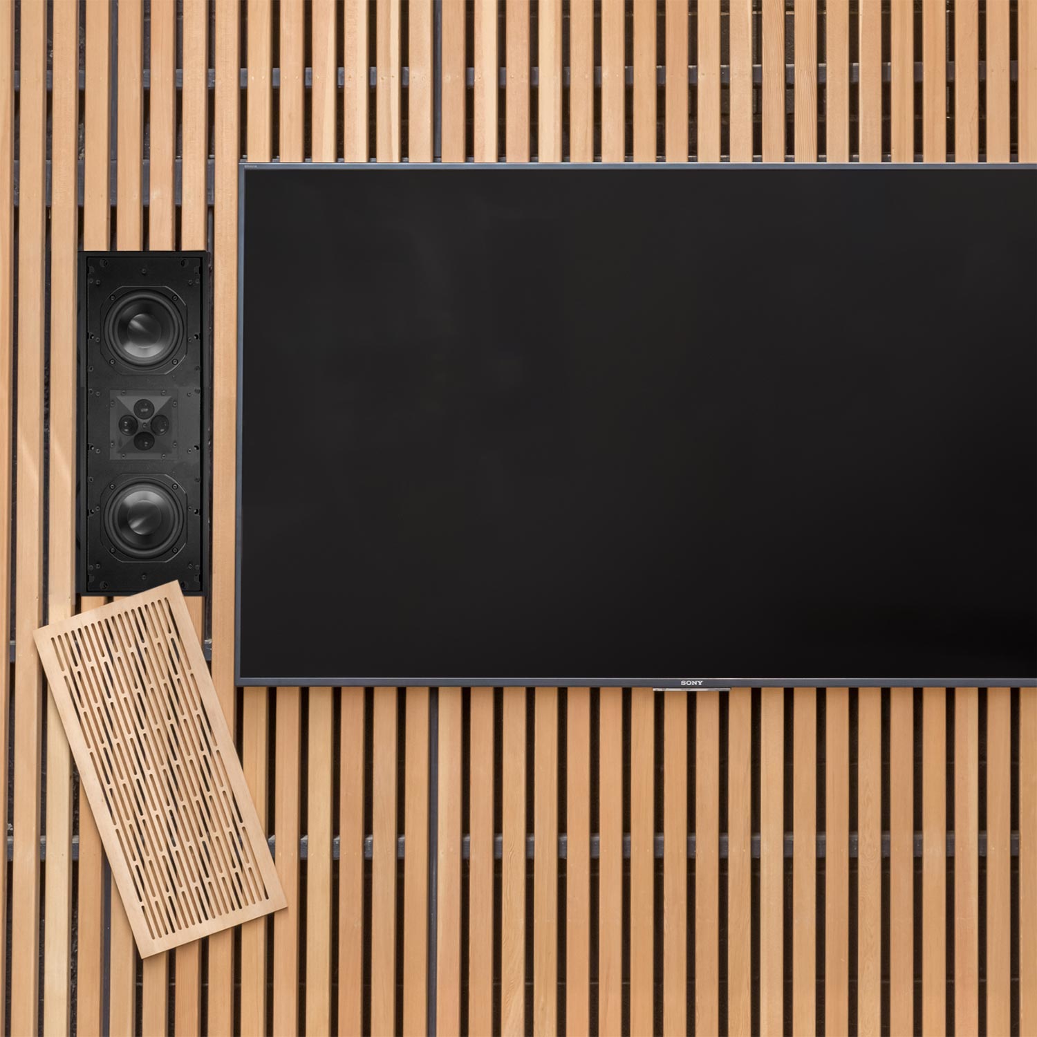 In-wall speaker with a custom wood slat grille next to a flat-screen television