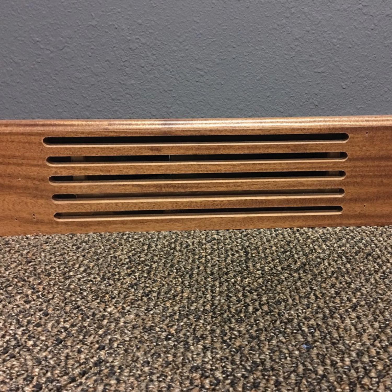 Subwoofer vent integrated into a wooden baseboard above patterned carpet