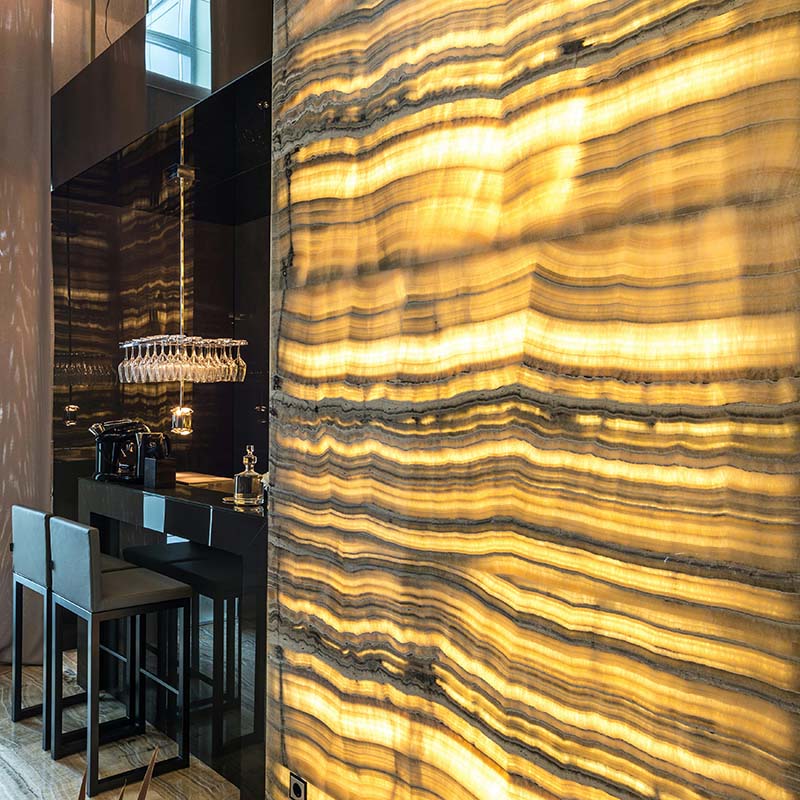 Vertical onyx panel illuminated from behind, showcasing intricate natural patterns in a refined interior setting.